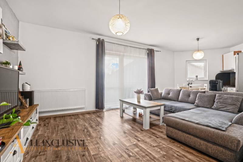 Nappali egy kétszobás lakásban fa dekor padlóval és szürke kanapéval.