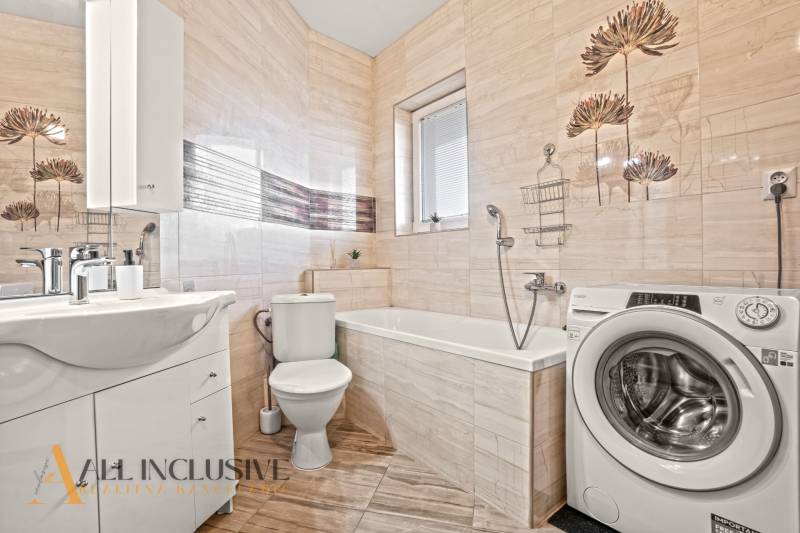 Fürdőszoba egy kétszobás lakásban mosógéppel, káddal, mosdóval és csempézett falakkal.