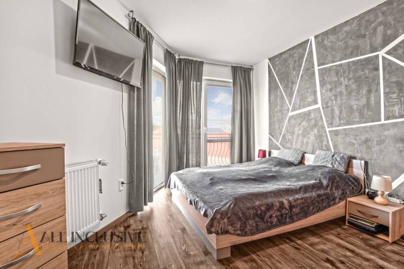 Hálószoba egy kétszobás lakásban, televízióval, ággyal és fa dekorációjú padlóval.