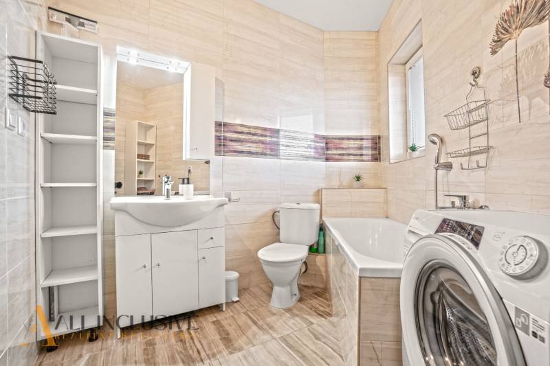 Fürdőszoba zuhanyzóval, káddal és mosógéppel egy kétszobás lakásban, fa hatású padlóval.