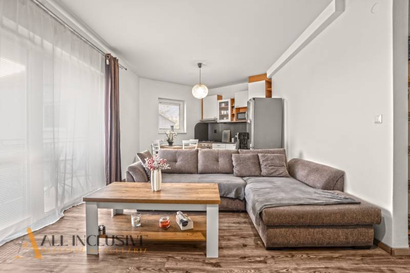 Nappali egy kétszobás lakásban kanapéval, konyhapulttal és fa dekorációjú padlóval.