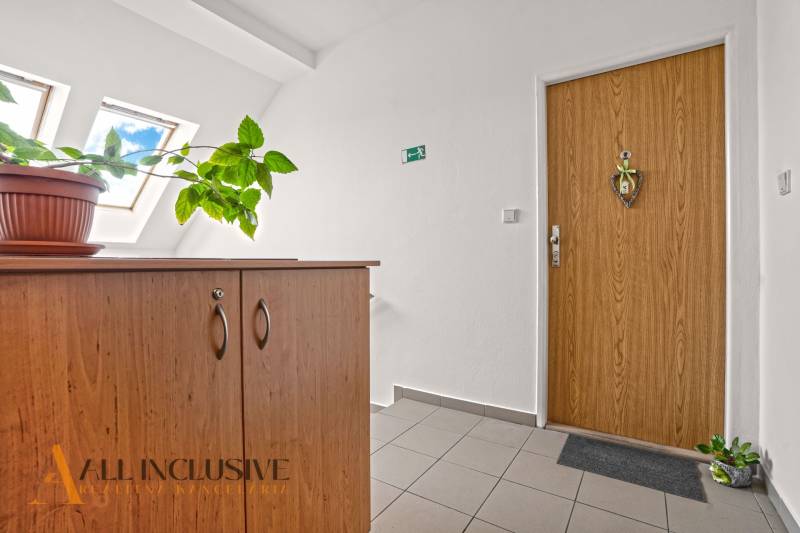 Belépés egy kétszobás lakásba, fa szekrénnyel és egy virággal a fapadlón.