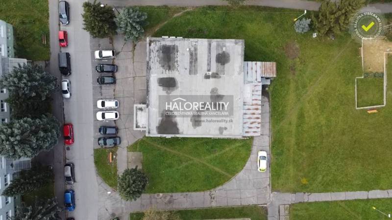 Kilátás Rimavská Sobota üzlethelyiségeire, amelyeket zöldterület és parkoló autók vesznek körül.