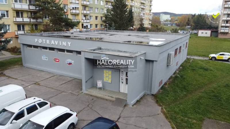 Egy üzlethelyiség épülete Rimaszombatban, panelházakkal és parkoló autókkal körülvéve.