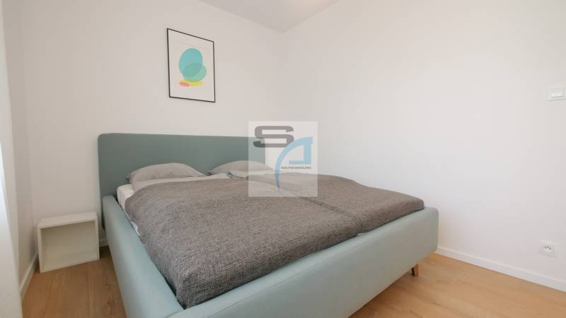 Hálószoba ággyal és minimalista dekorációval egy kétszobás lakásban, fa mintázatú padlóval.