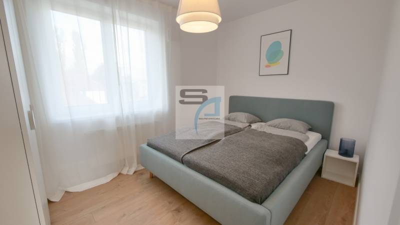 Hálószoba nagy ággyal, függönyökkel és fa dekorációjú padlóval egy kétszobás lakásban.