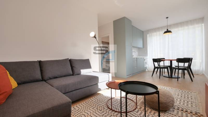 Nappali egy kétszobás lakásban kanapéval, étkezőasztallal és fa dekoros padlóval.