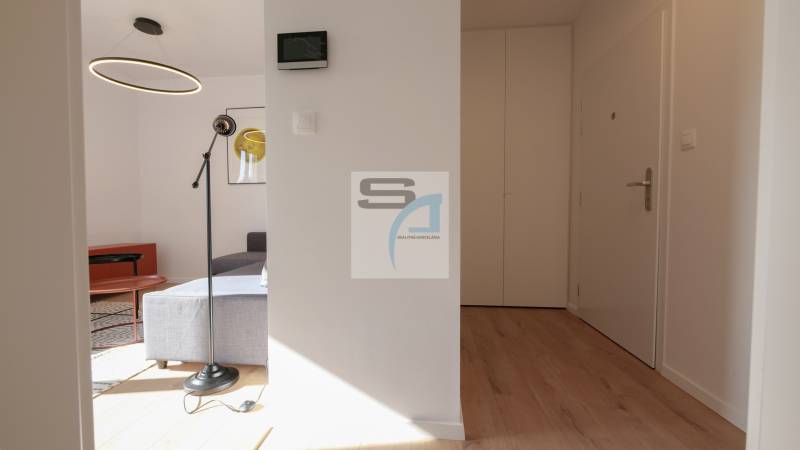 2 szobás lakás belső tere fa dekor padlóval, kör alakú csillárral és szürke kanapéval.