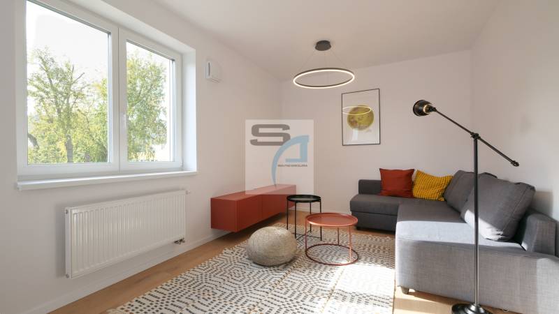 Nappali egy kétszobás lakásban, ülőhelyek, színes párnák, dohányzóasztalok, szőnyeg.