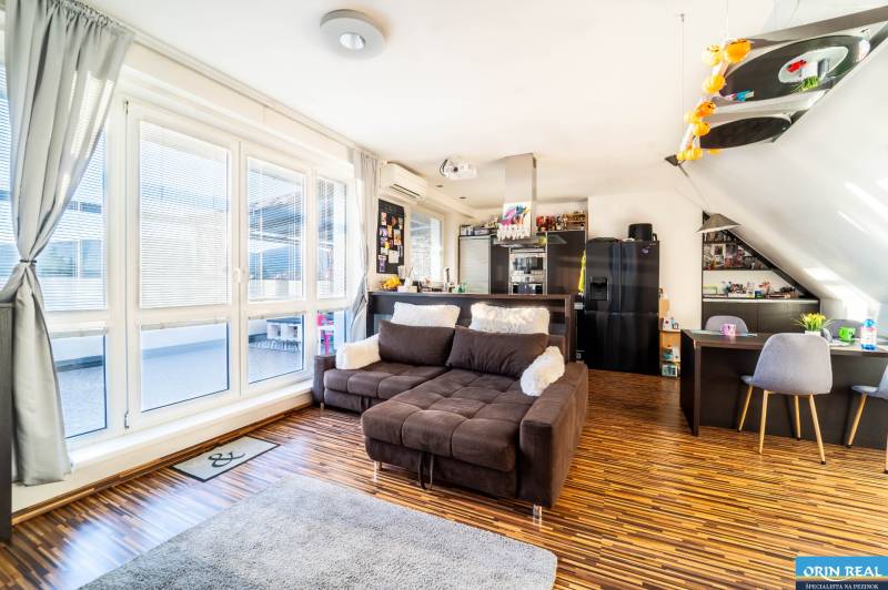 Nappali kényelmes kanapéval, fa mintázatú padlóval és nagy ablakokkal egy kétszobás lakásban.