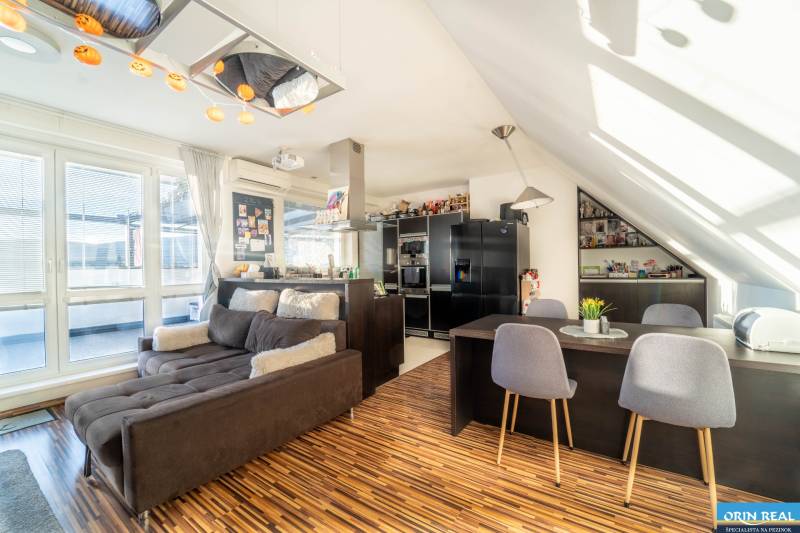 Nappali konyhával egy kétszobás lakásban, fa hatású padlóval és kényelmes kanapéval.