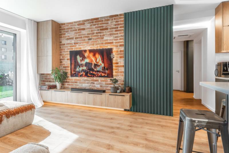 Nappali egy háromszobás lakásban téglafallal, kandallóval és fa mintázatú padlóval.