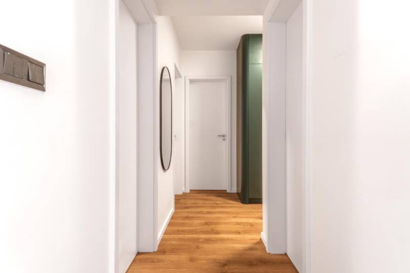 Keskeny belső tér fa dekor padlóval és egyszerű fehér fallal egy háromszobás lakásban.