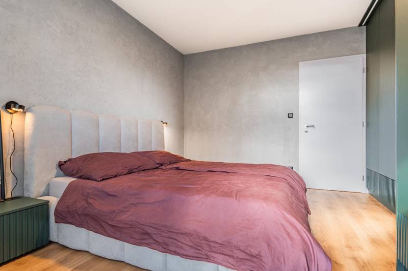 Hálószoba ággyal egy háromszobás lakásban, szürke falak, fa dekoros padló.