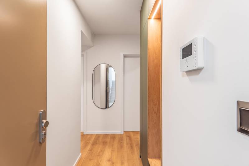 A háromszobás lakás folyosóján van egy tükör és fa dekorációjú padló.