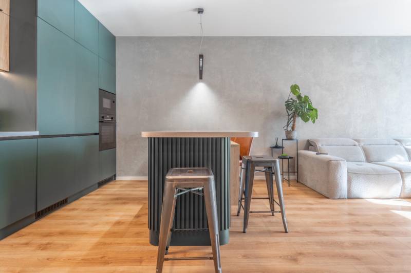 Konyha háromszobás lakásban szigettel, fém székekkel és fa mintázatú padlóval.