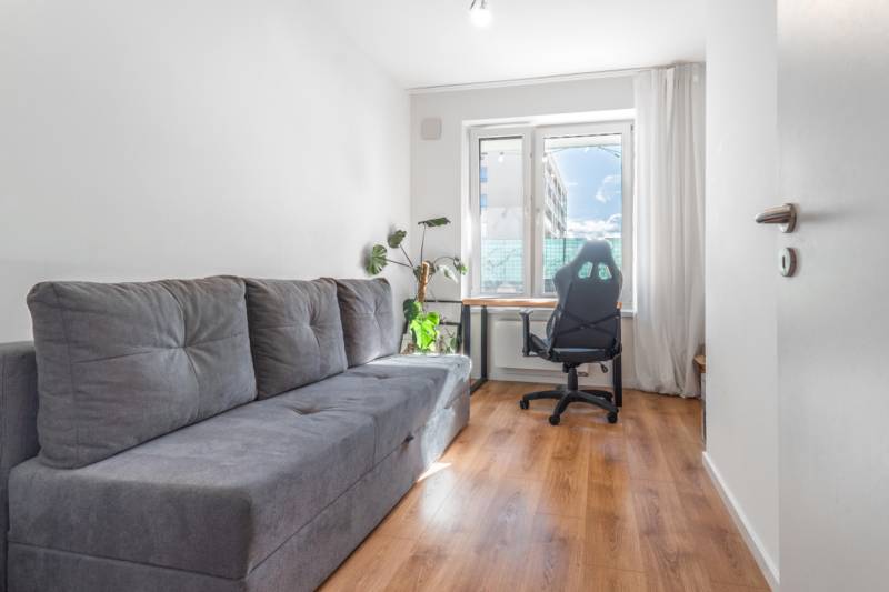 Világos szoba kanapéval, irodai székkel, asztallal és fa dekorációjú padlóval.