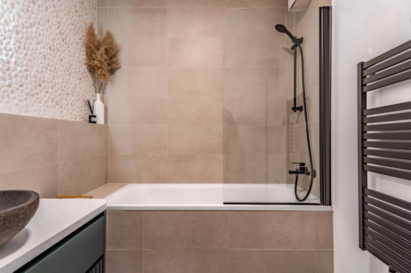 Fürdőszoba káddal, zuhanyfallal és dekoratív csempékkel egy háromszobás lakásban.