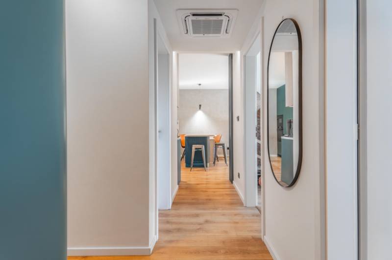 3 szobás lakás belső tere fa mintázatú padlóval és kerek tükörrel.