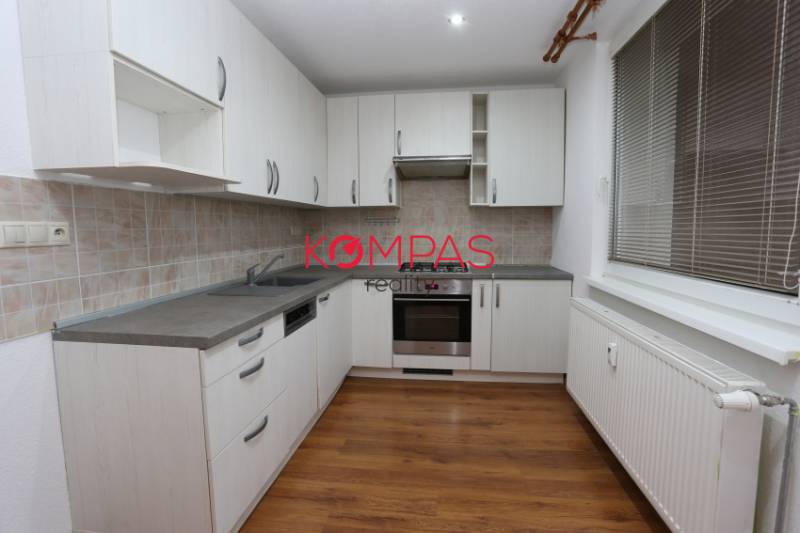 Konyha egy háromszobás lakásban fehér szekrényekkel és fa mintázatú padlóval.