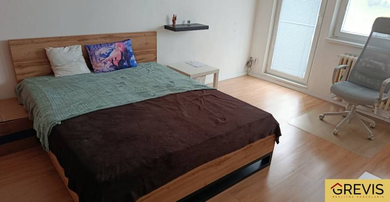 Hálószoba egy egyszobás lakásban fa dekor padlóval, ággyal és irodai székkel.