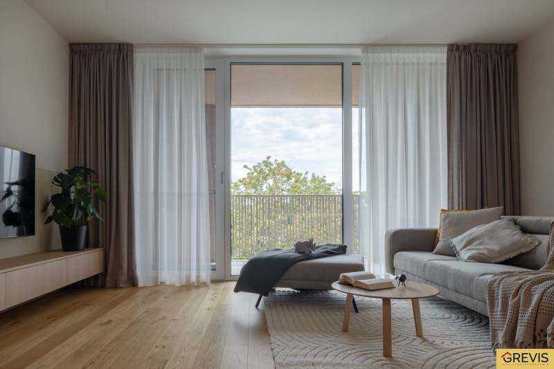 Nappali kanapéval, fa dekoros padlóval és nagy ablakkal egy háromszobás lakásban.