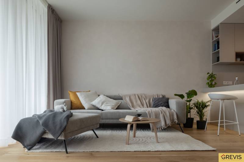 Nappali egy háromszobás lakásban kanapéval, asztallal, növényekkel és fa dekorációjú padlóval.