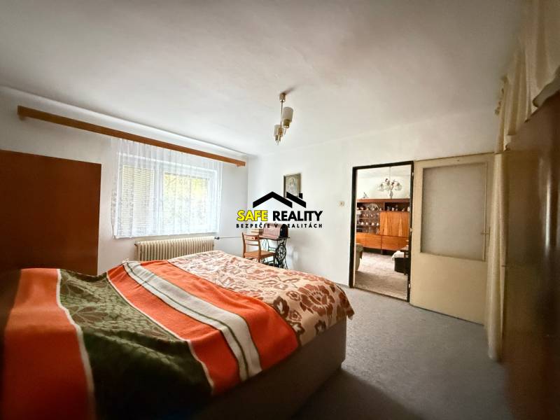 Hálószoba családi házban világos szőnyeggel, ablakkal és takaróval ellátott ággyal.