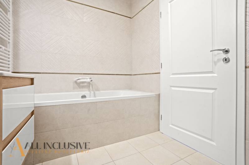 Fürdőszoba káddal, fehér ajtókkal és világos csempékkel egy kétszobás lakásban.