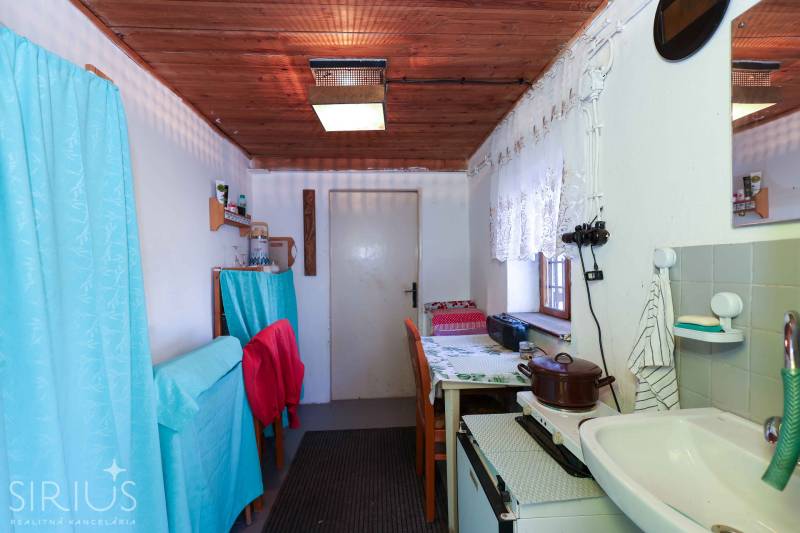 Konyhasarok a kertben függönyökkel, fából készült mennyezettel és egyszerű felszereléssel.