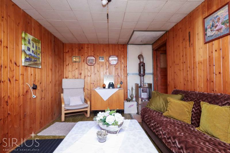 Belső tér fa burkolatú falakkal, cserépkályhával és retro bútorokkal a kertekben.