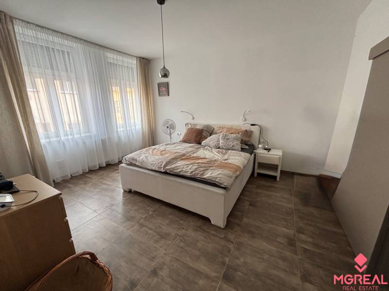 Hálószoba egy kétszobás lakásban nagy ablakokkal, ággyal és fa dekorációjú padlóval.