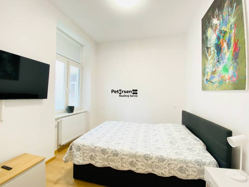 Hálószoba televízióval, ággyal és absztrakt festménnyel egy kétszobás lakásban.