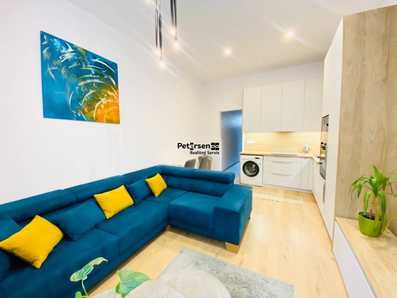 Nappali egy kétszobás lakásban kék kanapéval és fa dekorációjú padlóval.