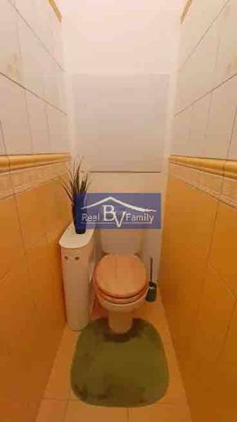 Bézs falakkal és csempékkel rendelkező WC egy kétszobás lakásban dekorációval.