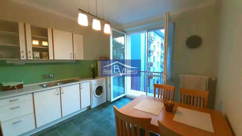 Konyha egy kétszobás lakásban fehér szekrényekkel, étkezőasztallal és erkéllyel.