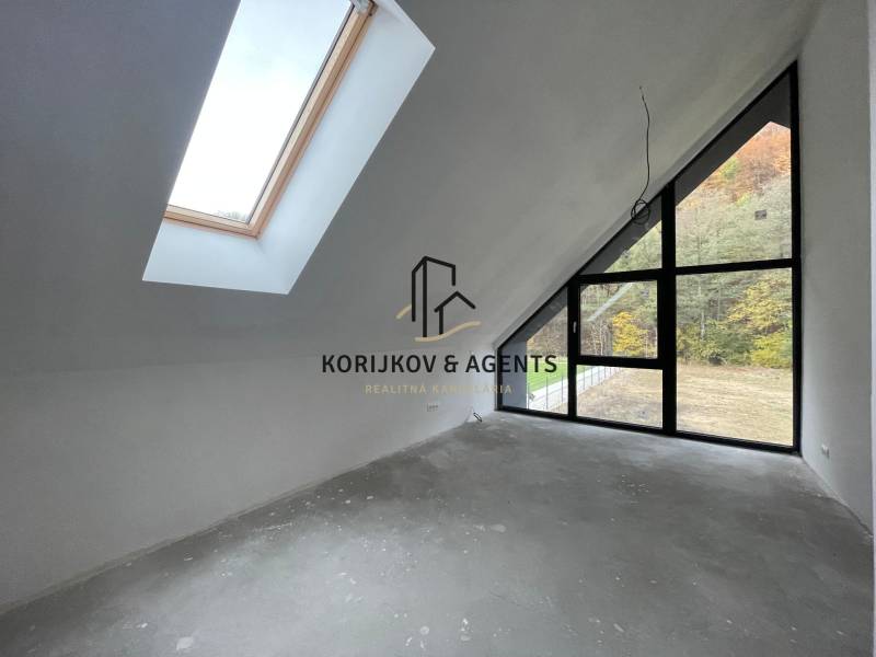 Tetőtéri szoba egy családi házban nagy ablakokkal és kilátással az erdőre.