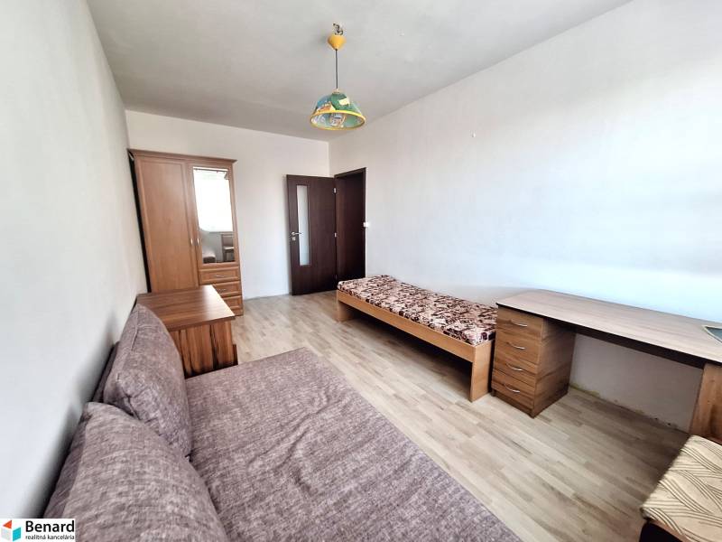 Szoba egy háromszobás lakásban, fa dekorációjú padlóval, ággyal és szekrénnyel.