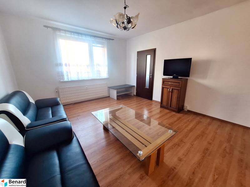 Nappali kanapéval, asztallal és televízióval, fa dekorációjú padlóval egy háromszobás lakásban.