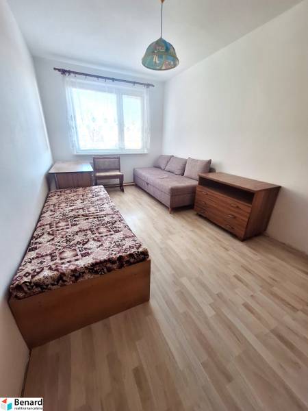 Szoba egy háromszobás lakásban, fa dekorációjú padlóval, székkel és ággyal.