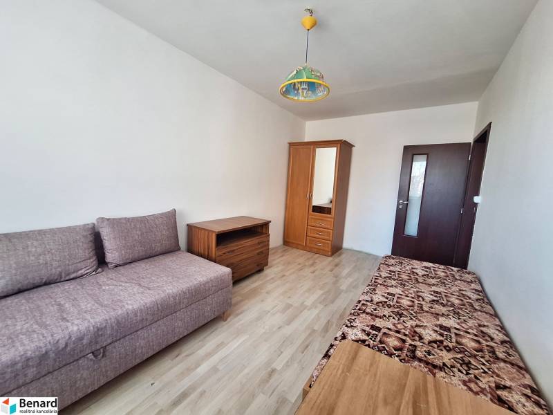 Nappali egy háromszobás lakásban, fa dekor padlóval és egyszerű bútorokkal.