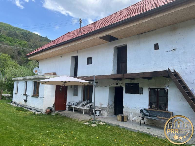 Vidéki ház piros tetővel és terasszal, zöld gyep és természet veszi körül.