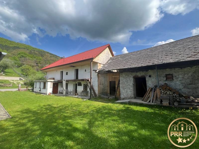 Vidéki házak piros tetővel, köves külső, zöld gyep, erdő és kék ég.