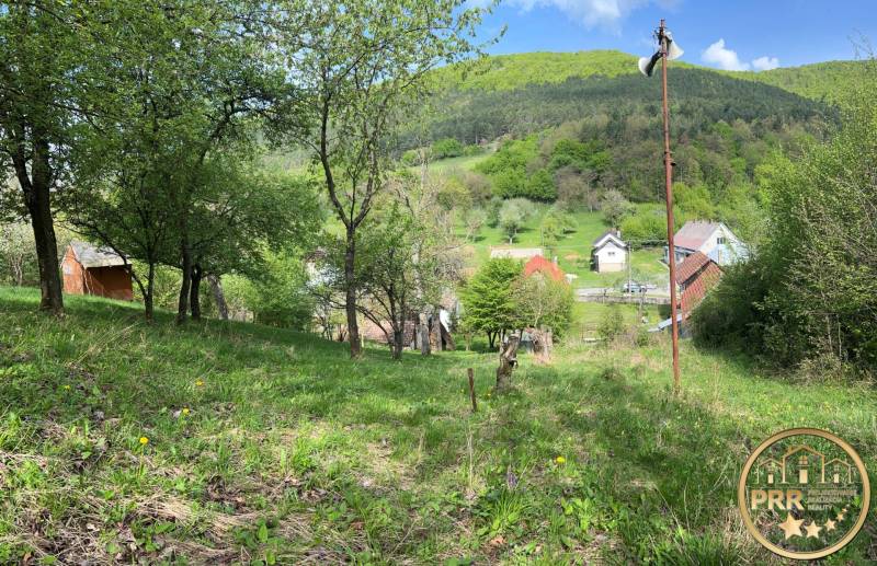 Gyönyörű természeti táj házikóval, fákkal és festői falucskával a völgy hátterében.