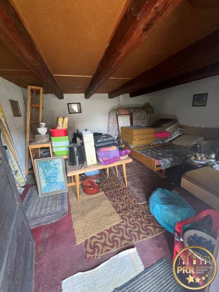 Egy használaton kívüli kunyhó belseje vidéki bútorokkal és mennyezeti gerendákkal.