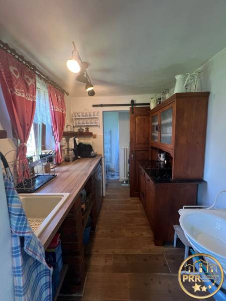 Konyha egy faházban rusztikus bútorokkal, mosogatóval és dekoratív függönyökkel.