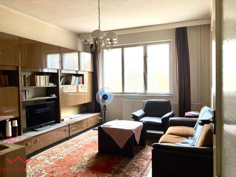 Nappali egy háromszobás lakásban bútorokkal, szőnyeggel és nagy ablakkal.