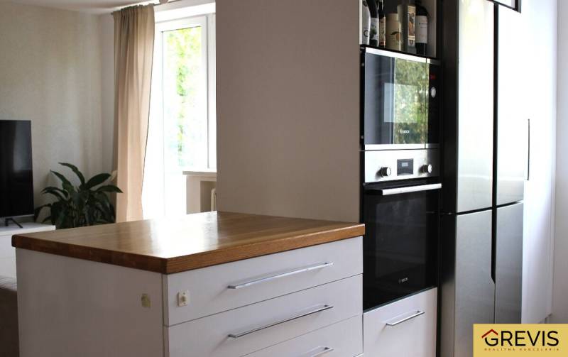 Konyha egy háromszobás lakásban, sötét szekrény beépített sütővel, mellette hűtőszekrény.