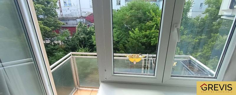 Kilátás egy 3 szobás lakásból, ablakokkal és erkéllyel a zöld udvarra.