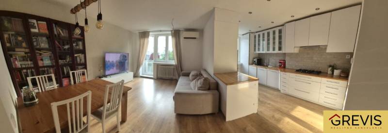 Tágas konyha nappalival egy háromszobás lakásban. Fa hatású padló, világos bútorok.